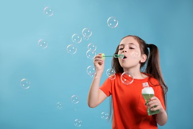 Photo of Little girl blowing soap bubbles on light blue background, space for text