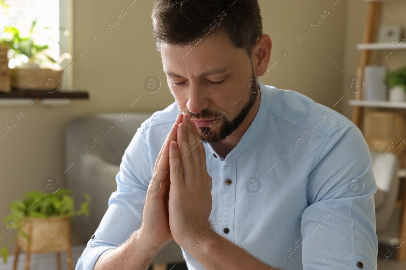 Religious man with clasped hands praying indoors Photo of Religious man with clasped hands praying indoors
