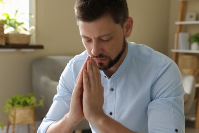Religious man with clasped hands praying indoors Photo of Religious man with clasped hands praying indoors