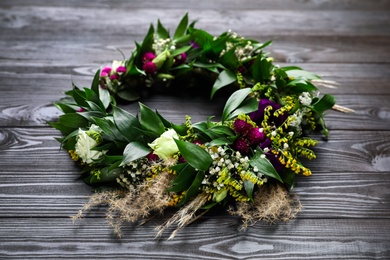 Beautiful wreath made of flowers and leaves on wooden table Photo of Beautiful wreath made of flowers and leaves on wooden table