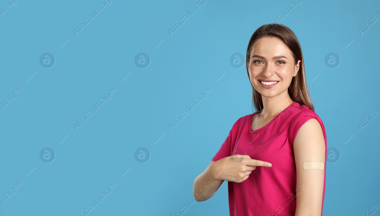 Vaccinated woman showing medical plaster on her arm against light blue background Photo of Vaccinated woman showing medical plaster on her arm against light blue background