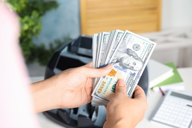 Woman holding money near counting machine indoors, closeup Photo of Woman holding money near counting machine indoors, closeup