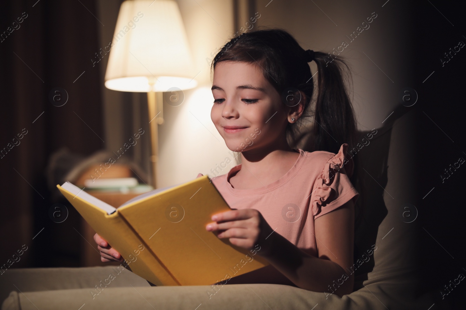 Photo of Little girl reading fairy tale at home in evening