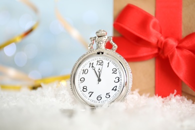 Pocket watch and gift on snow against blurred lights. New Year countdown Photo of Pocket watch and gift on snow against blurred lights. New Year countdown