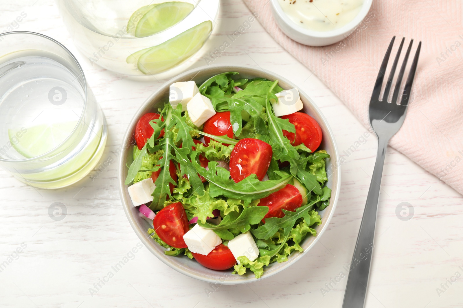 Delicious salad with arugula and vegetables on white table, flat lay Photo of Delicious salad with arugula and vegetables on white table, flat lay