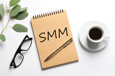 Notebook with abbreviation SMM, cup of coffee and glasses on white background, flat lay. Social media marketing Image of Notebook with abbreviation SMM, cup of coffee and glasses on white background, flat lay. Social media marketing
