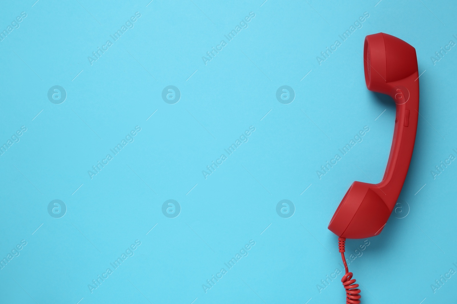 Red corded telephone handset on light blue background, top view. Hotline concept Photo of Red corded telephone handset on light blue background, top view. Hotline concept