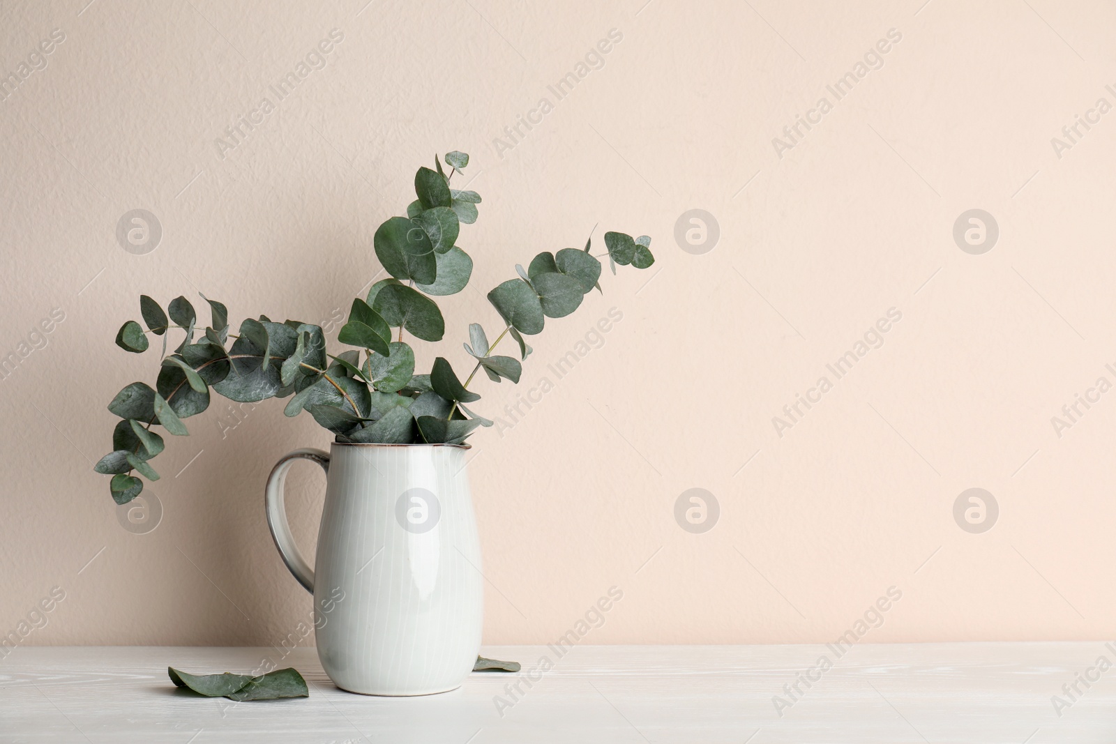 Vase with beautiful eucalyptus branches on white wooden table near beige wall. Space for text Photo of Vase with beautiful eucalyptus branches on white wooden table near beige wall. Space for text