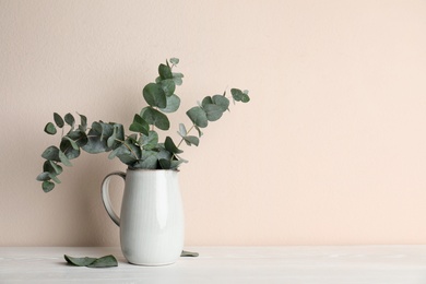 Vase with beautiful eucalyptus branches on white wooden table near beige wall. Space for text Photo of Vase with beautiful eucalyptus branches on white wooden table near beige wall. Space for text