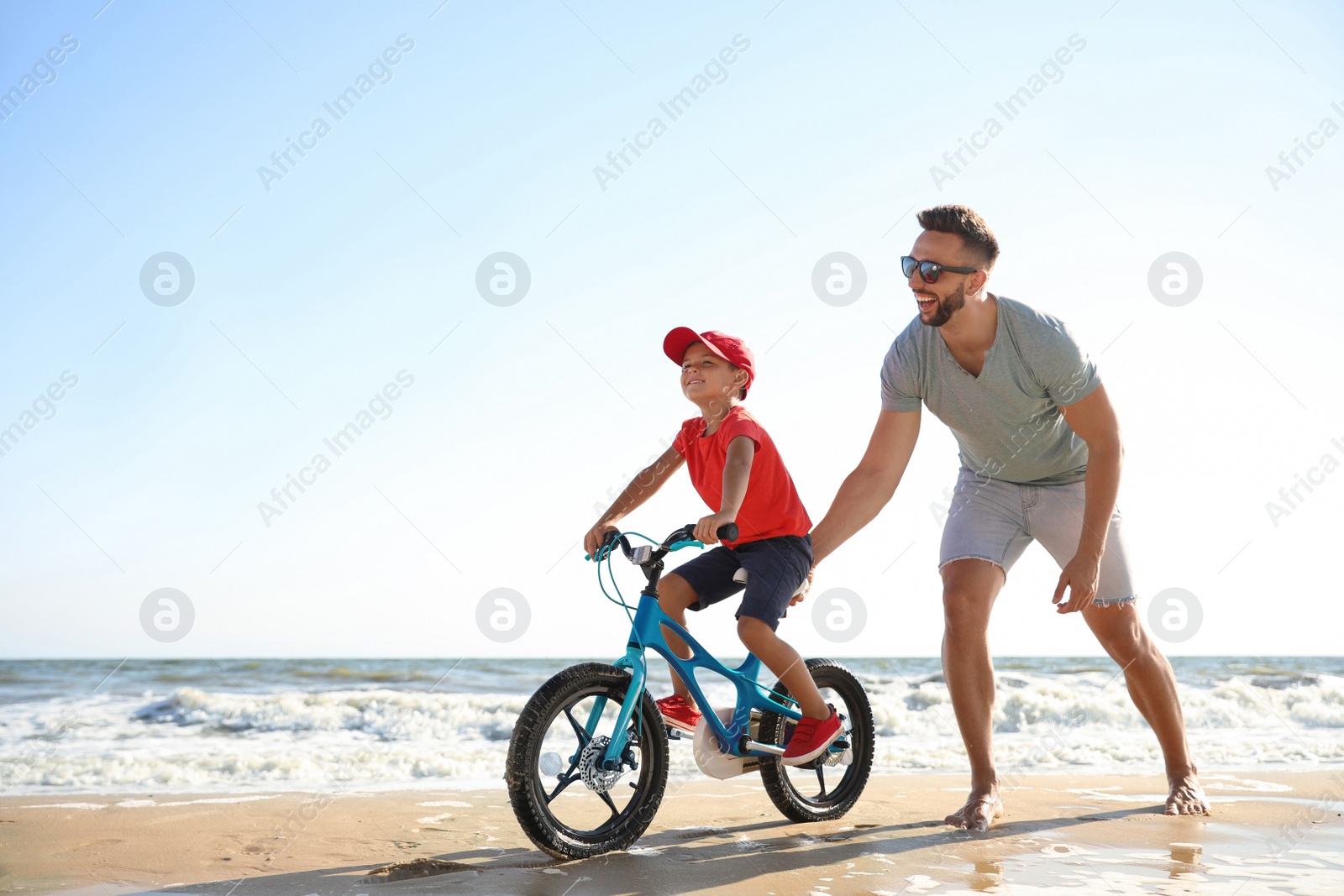 Photo of Happy father teaching son to ride bicycle on sandy beach near sea