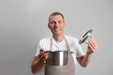 Happy man with cooking pot on light grey background Photo of Happy man with cooking pot on light grey background