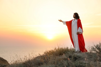 Jesus Christ raising hand on hills at sunset. Space for text Photo of Jesus Christ raising hand on hills at sunset. Space for text