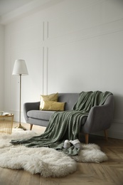 Stylish room interior with comfortable sofa, knitted blanket and lamp near white wall Photo of Stylish room interior with comfortable sofa, knitted blanket and lamp near white wall