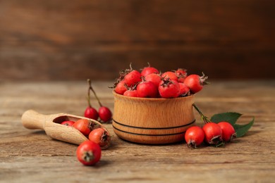 Ripe rose hip berries with green leaves and scoop on wooden table Photo of Ripe rose hip berries with green leaves and scoop on wooden table