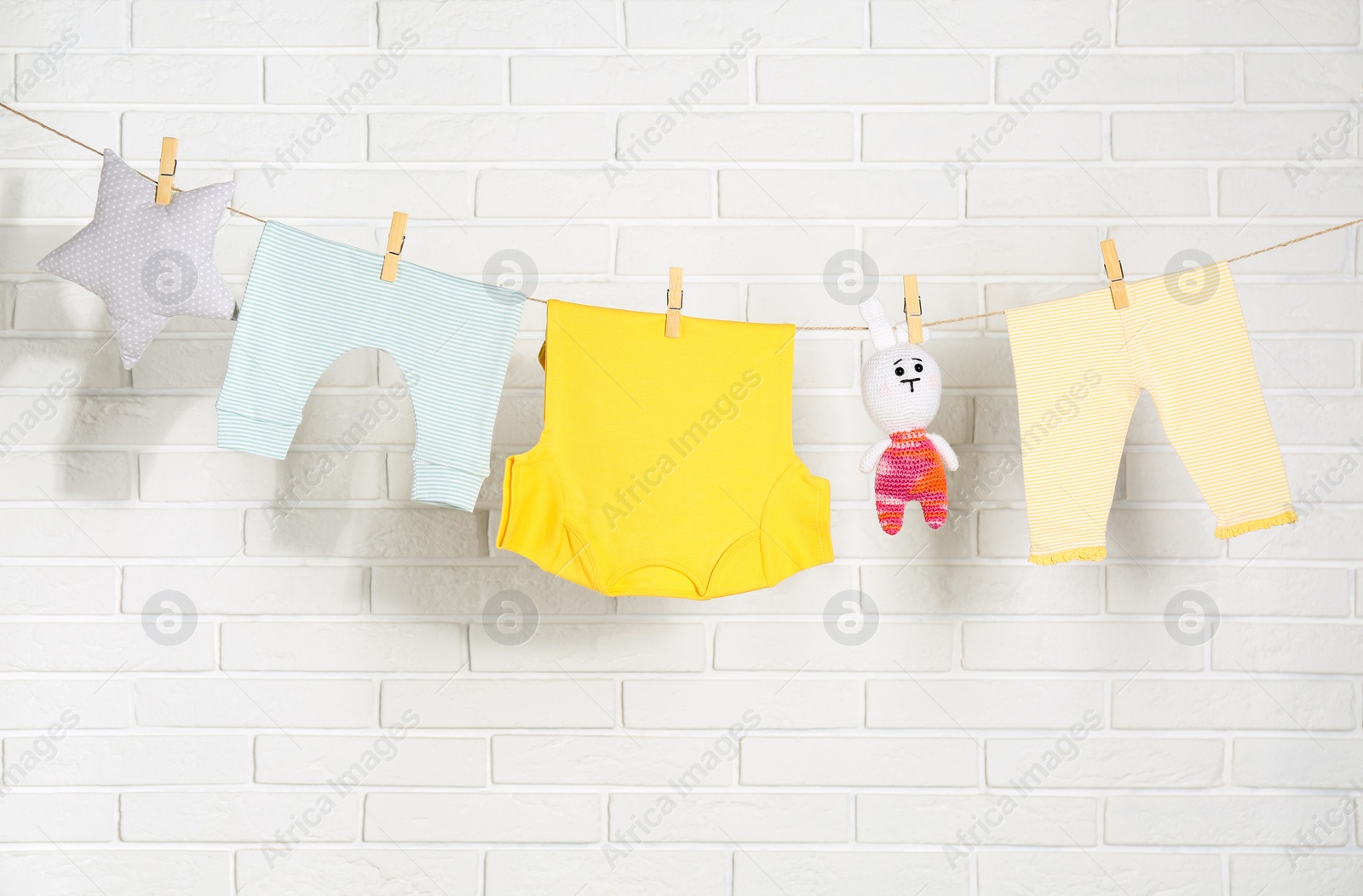 Baby clothes hanging on washing line near white brick wall Photo of Baby clothes hanging on washing line near white brick wall
