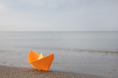 Orange paper boat on sandy beach near sea, space for text Photo of Orange paper boat on sandy beach near sea, space for text