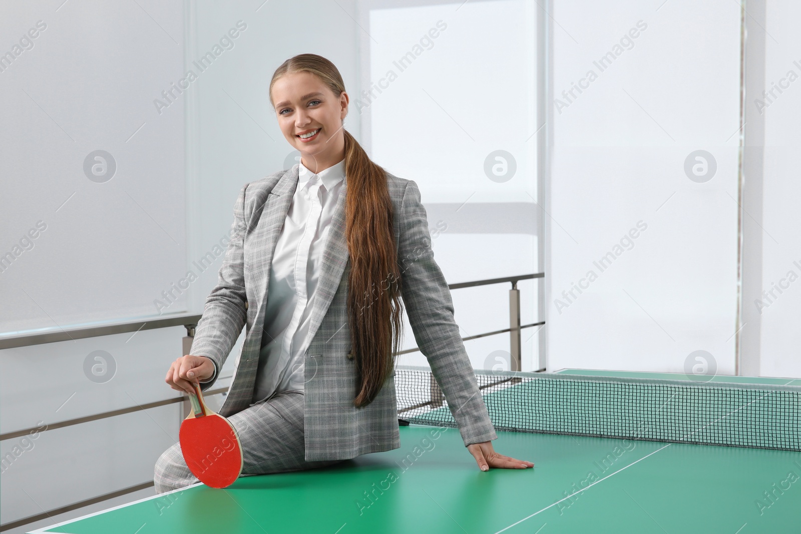Business woman with tennis racket near ping pong table in office. Space for text Photo of Business woman with tennis racket near ping pong table in office. Space for text