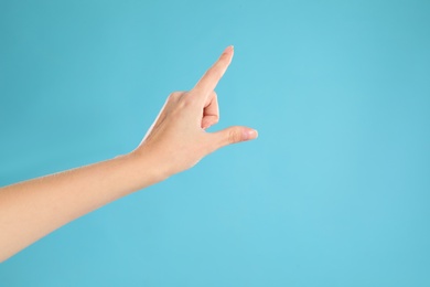 Woman pointing at something on light blue background, closeup. Finger gesture Photo of Woman pointing at something on light blue background, closeup. Finger gesture