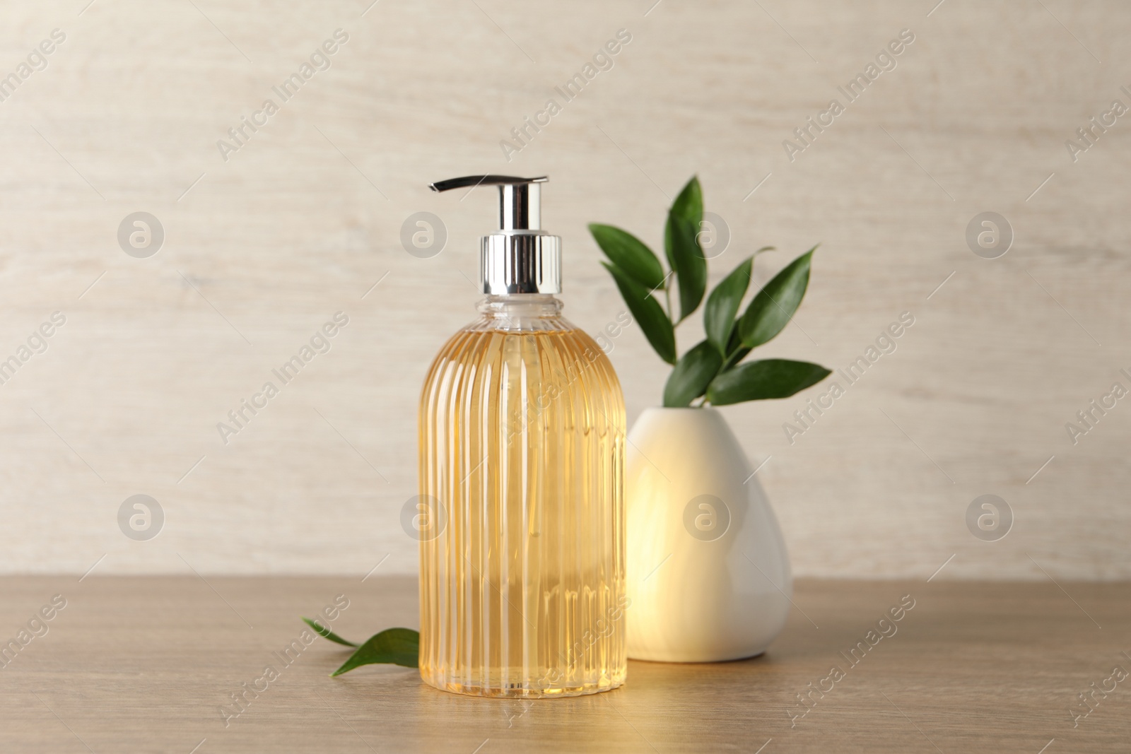 Stylish dispenser with liquid soap and green leaves in vase on wooden table Photo of Stylish dispenser with liquid soap and green leaves in vase on wooden table