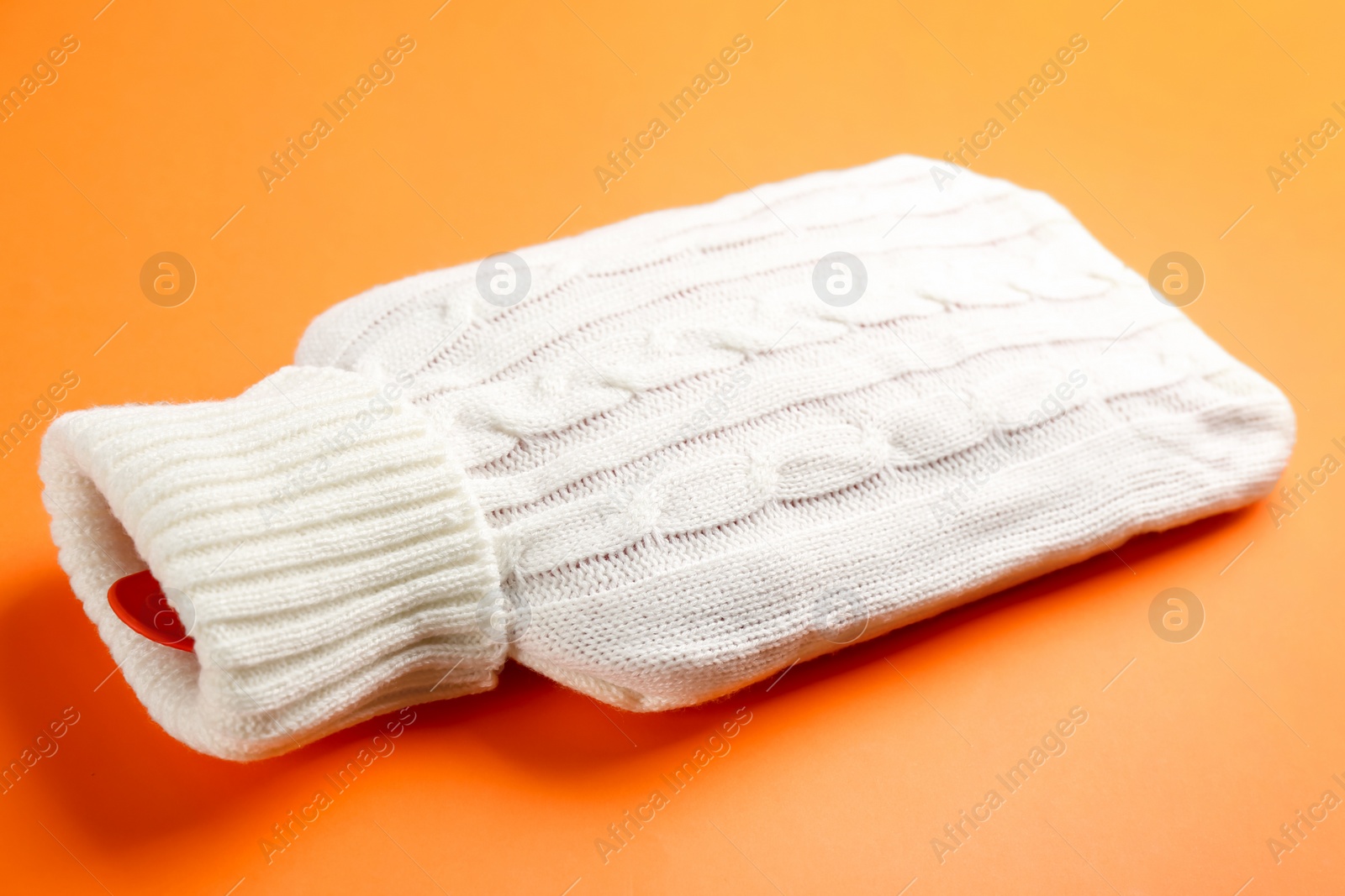 Photo of Hot water bottle with knitted cover on orange background, closeup