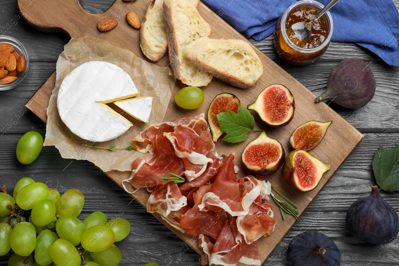 Board with delicious figs, proscuitto, cheese and grapes on grey wooden table, flat lay Photo of Board with delicious figs, proscuitto, cheese and grapes on grey wooden table, flat lay