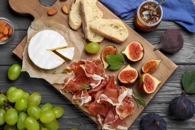 Board with delicious figs, proscuitto, cheese and grapes on grey wooden table, flat lay Photo of Board with delicious figs, proscuitto, cheese and grapes on grey wooden table, flat lay