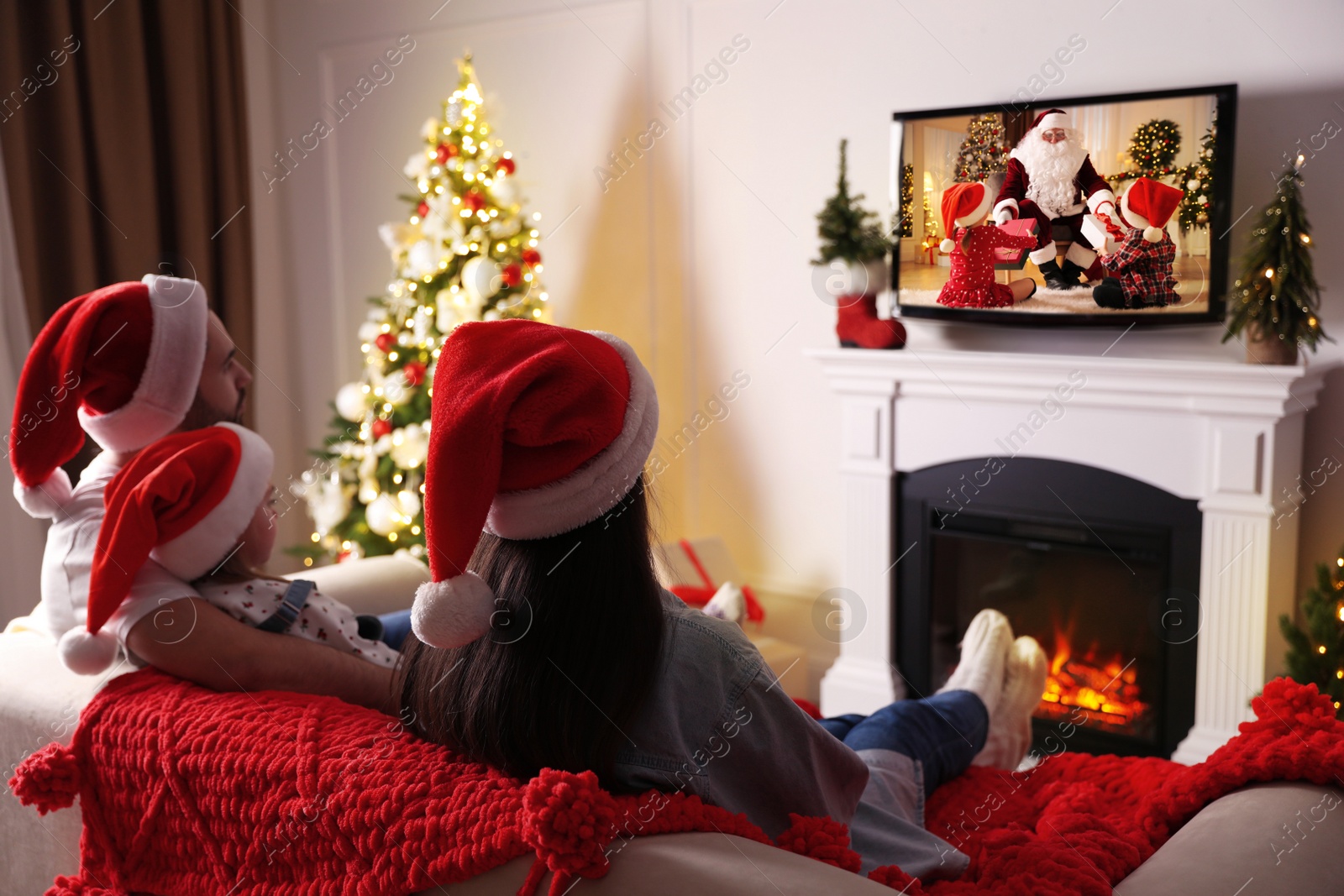 Family watching festive movie on TV in room decorated for Christmas Image of Family watching festive movie on TV in room decorated for Christmas