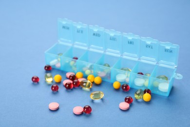 Plastic box with different pills on light blue background Photo of Plastic box with different pills on light blue background