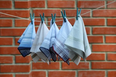 Photo of Different handkerchiefs hanging on rope near red brick wall outdoors