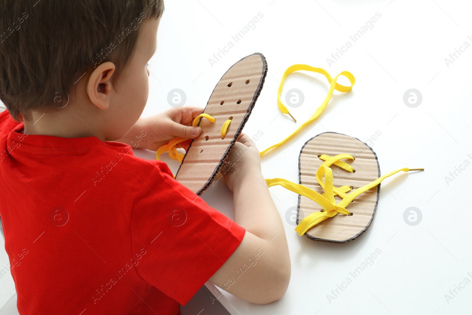 Little boy tying shoe laces using training cardboard template at white table Photo of Little boy tying shoe laces using training cardboard template at white table