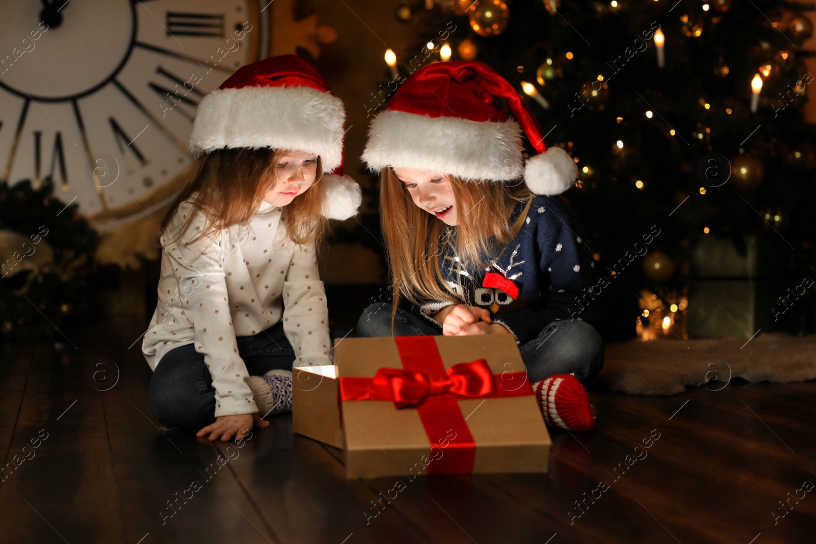 Cute children opening magic gift box near Christmas tree at night Photo of Cute children opening magic gift box near Christmas tree at night