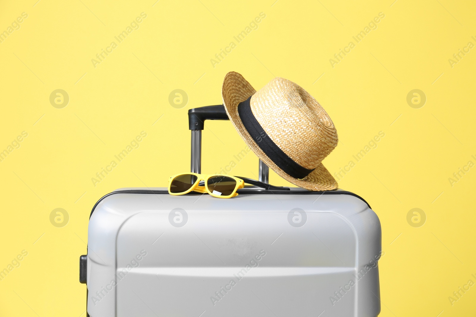 Photo of Grey suitcase with sunglasses and hat on yellow background