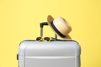 Photo of Grey suitcase with sunglasses and hat on yellow background