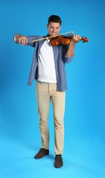 Happy man playing violin on light blue background Photo of Happy man playing violin on light blue background