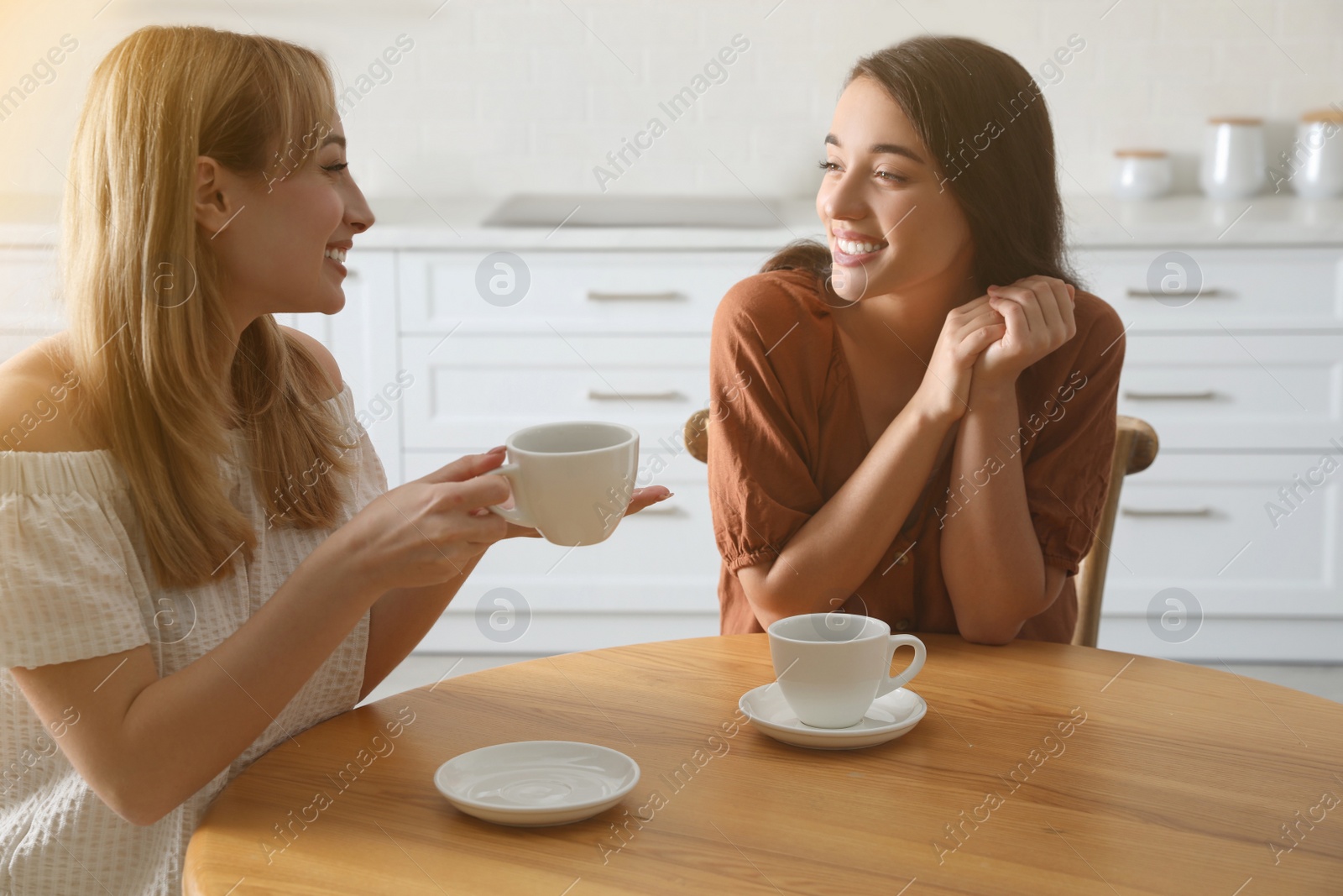 Young women talking while drinking tea at table in kitchen Photo of Young women talking while drinking tea at table in kitchen
