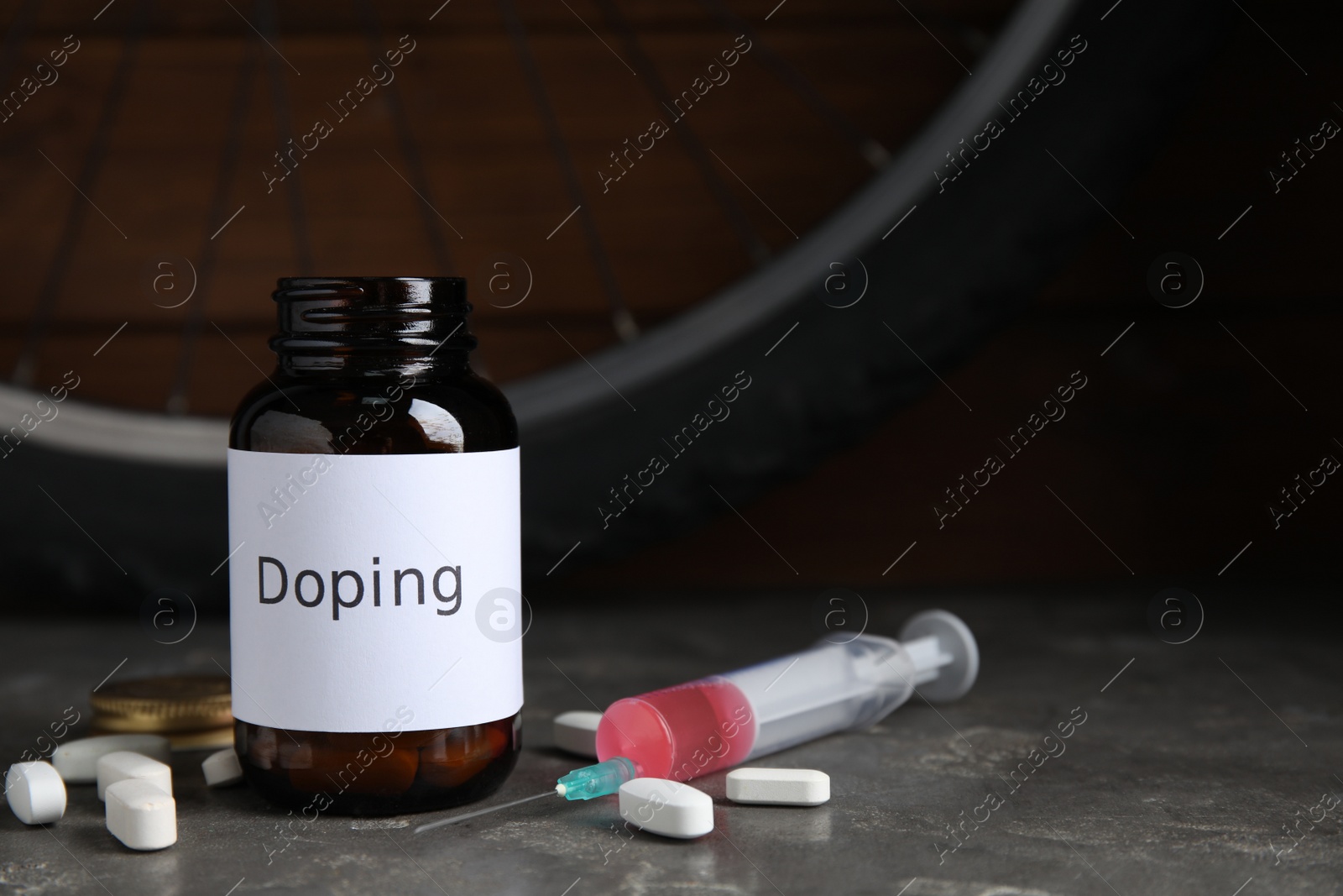Pills, syringe and bike wheel on grey table. Using doping in cycling sport concept Photo of Pills, syringe and bike wheel on grey table. Using doping in cycling sport concept