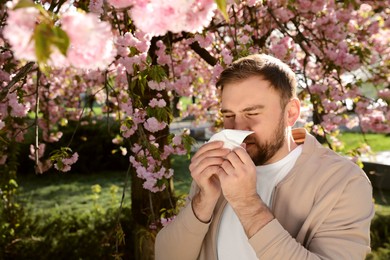 Man suffering from seasonal pollen allergy near blossoming tree outdoors Photo of Man suffering from seasonal pollen allergy near blossoming tree outdoors
