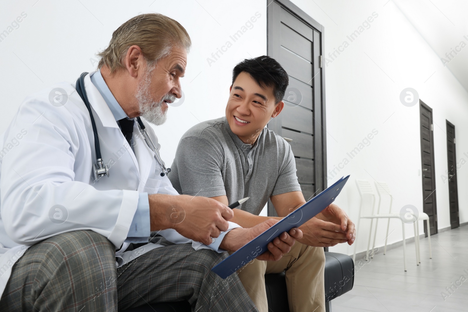 Senior doctor with clipboard consulting patient in clinic Photo of Senior doctor with clipboard consulting patient in clinic
