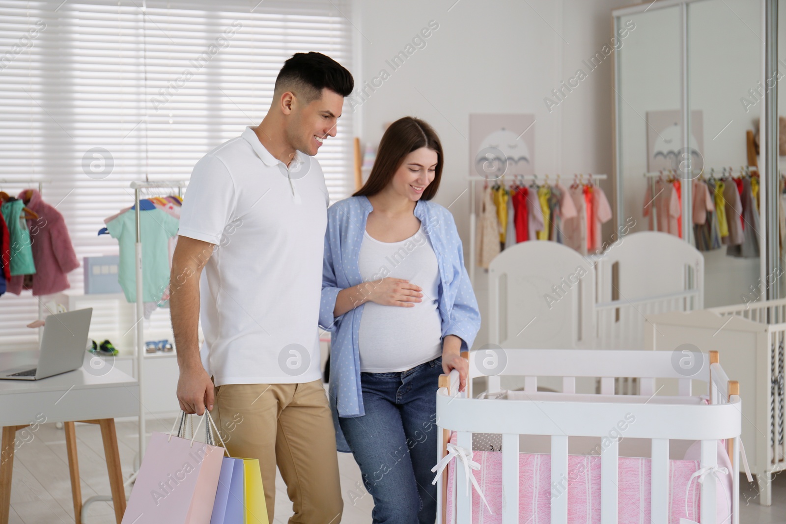 Happy pregnant woman and her husband with shopping bags choosing crib in store Photo of Happy pregnant woman and her husband with shopping bags choosing crib in store