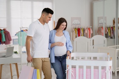 Happy pregnant woman and her husband with shopping bags choosing crib in store Photo of Happy pregnant woman and her husband with shopping bags choosing crib in store