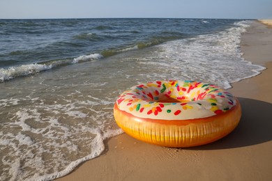 Inflatable ring with doughnut pattern on sandy beach near sea, space for text Photo of Inflatable ring with doughnut pattern on sandy beach near sea, space for text