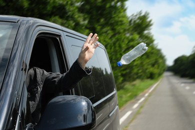 Driver throwing away plastic bottle from car window. Garbage on road Photo of Driver throwing away plastic bottle from car window. Garbage on road
