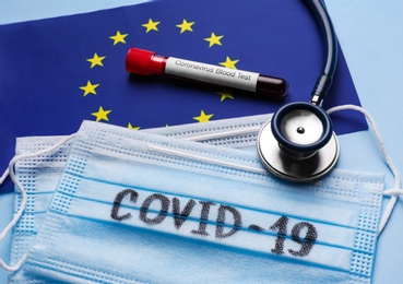 European Union flag, protective masks, stethoscope and test tube with blood sample on light blue background. Coronavirus outbreak Photo of European Union flag, protective masks, stethoscope and test tube with blood sample on light blue background. Coronavirus outbreak