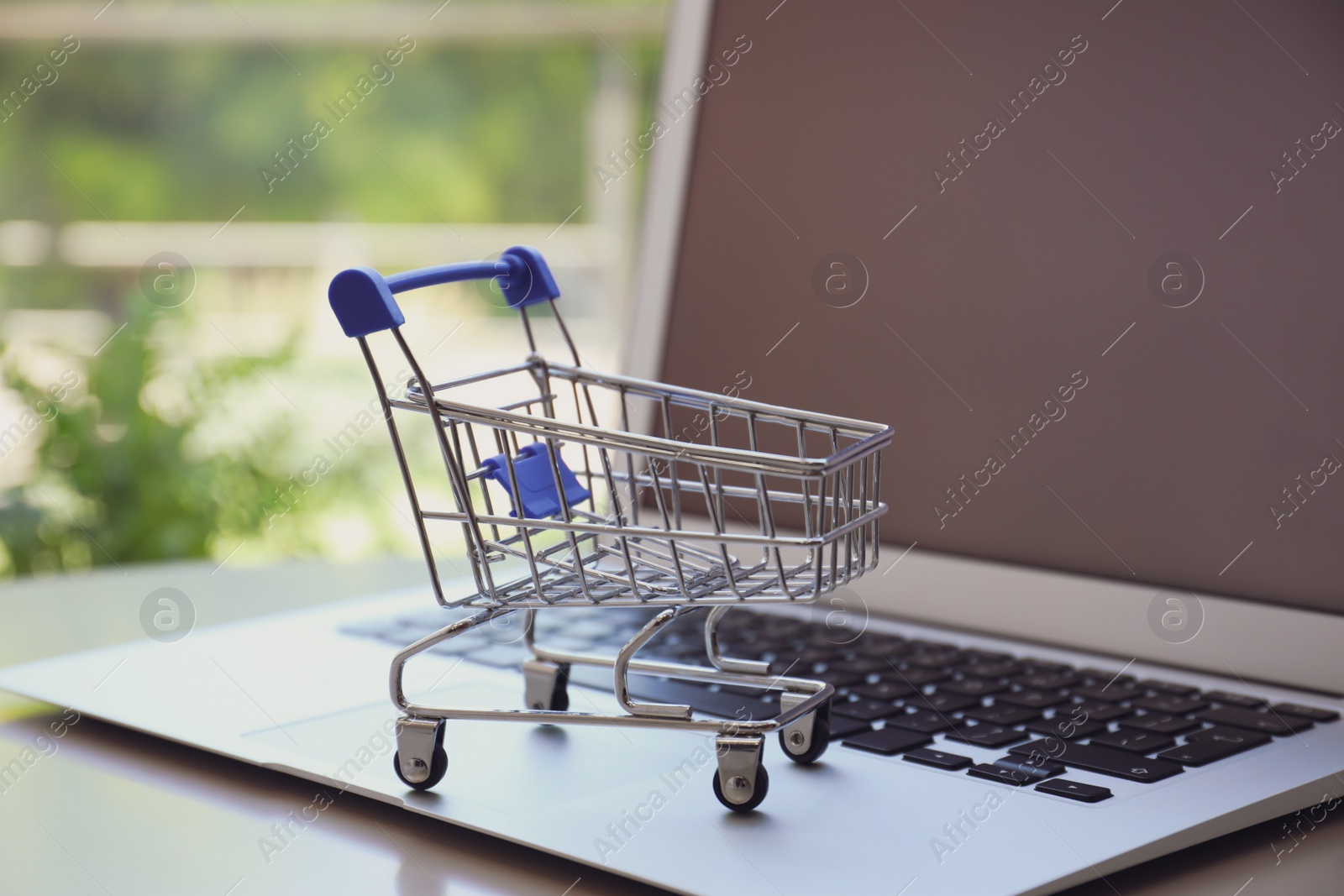 Internet shopping. Laptop with small cart on table indoors, closeup Photo of Internet shopping. Laptop with small cart on table indoors, closeup