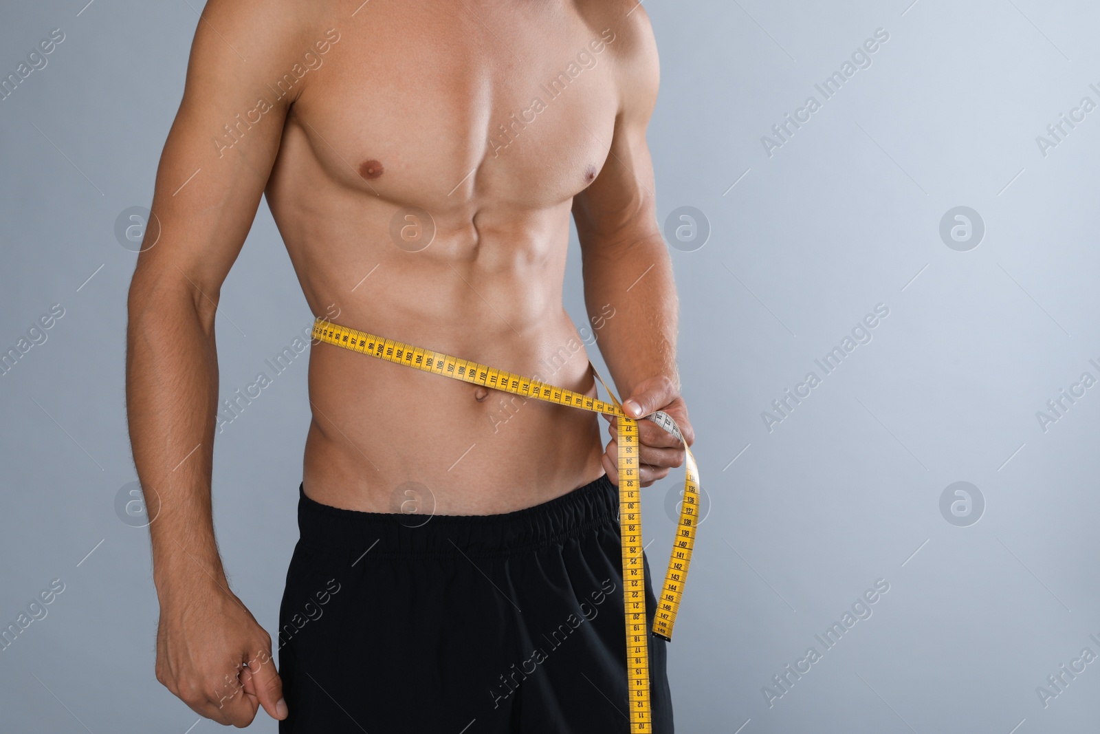 Shirtless man with slim body and measuring tape around his waist on grey background, closeup. Space for text Photo of Shirtless man with slim body and measuring tape around his waist on grey background, closeup. Space for text