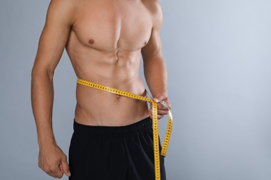 Shirtless man with slim body and measuring tape around his waist on grey background, closeup. Space for text Photo of Shirtless man with slim body and measuring tape around his waist on grey background, closeup. Space for text