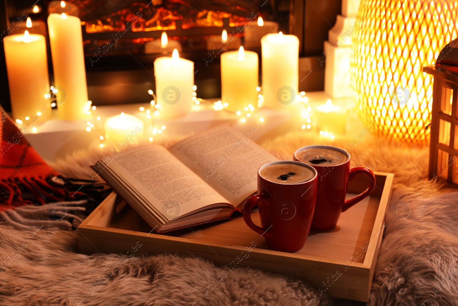 Cups of hot drink and open book near fireplace at home Photo of Cups of hot drink and open book near fireplace at home