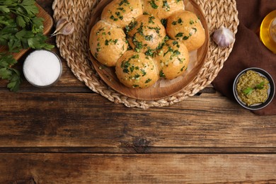 Traditional pampushka buns with garlic and herbs on wooden table, flat lay. Space for text Photo of Traditional pampushka buns with garlic and herbs on wooden table, flat lay. Space for text