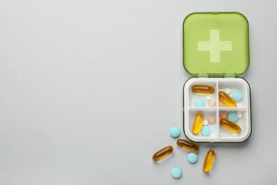 Plastic box with different pills on light grey background, flat lay. Space for text Photo of Plastic box with different pills on light grey background, flat lay. Space for text