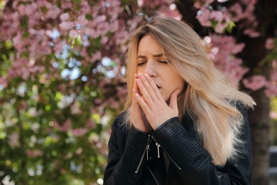 Woman suffering from seasonal pollen allergy near blossoming tree outdoors Photo of Woman suffering from seasonal pollen allergy near blossoming tree outdoors